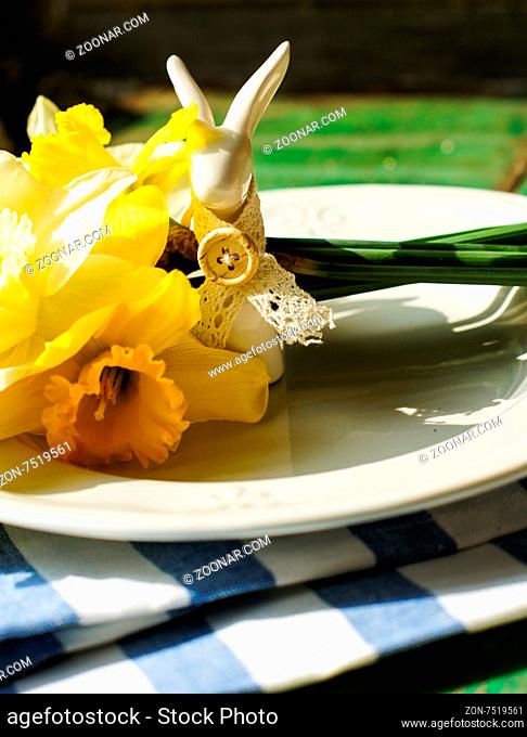 Spring festive easter dining table setting with yellow daffodil flowers, napkins and vintage cutlery on a wooden board