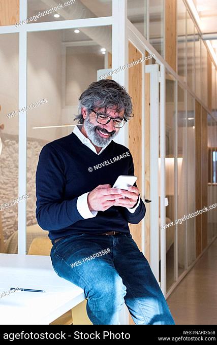 Happy senior man surfing net through mobile phone sitting on table at home