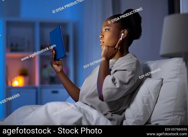woman with tablet pc and earphones in bed at night