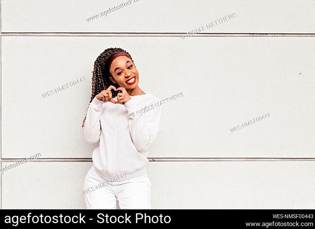 Happy beautiful woman gesturing heart shape in front of white wall
