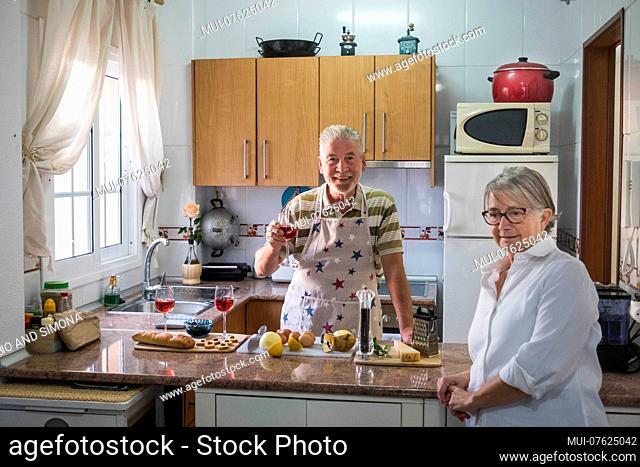 An adult senior man drink wine while prepare something to eat for a cocktail with her woman. Elderly home work in an usual kitchen