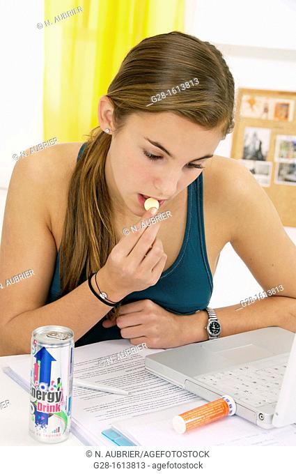 Teenage girl, doing her homework on her computer and eating a tablet of vitamin C, and drinking an energy drink