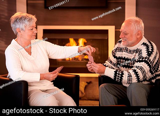 Senior couple playing cards on winter night in front of fireplace