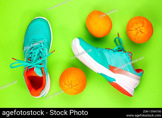 Red, cyan, white pair of new tennis shoes in studio shot over green background with oranges next to them. Directly from above