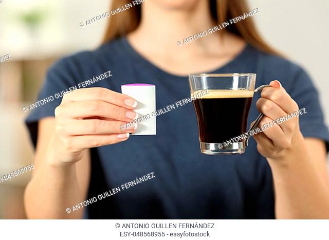 Front view close up of a woman hands holding a coffee cup and saccharin at home