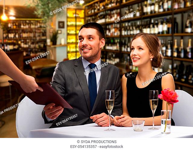 waiter giving menu to happy couple at restaurant