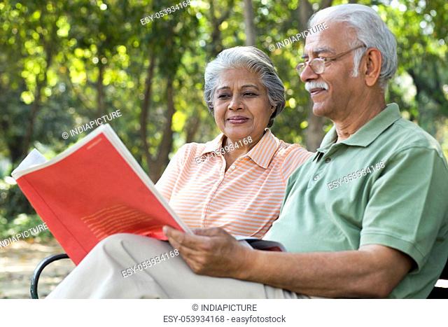 Relaxed senior man reading book with woman at park