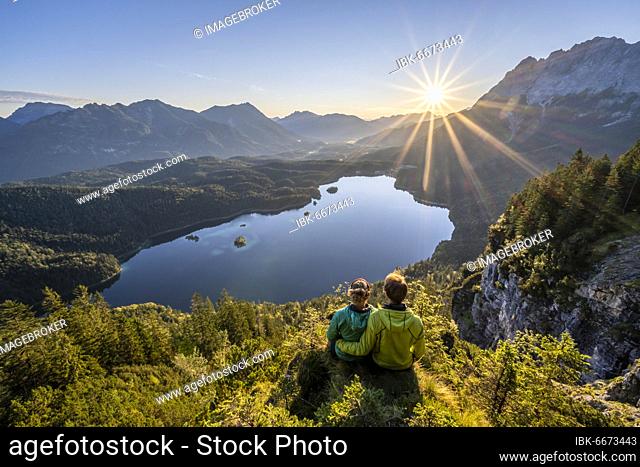 Two (hikers) looking at Eibsee lake at sunrise, sun shining over Bavarian alpine foothills, right Zugspitze, Wetterstein mountains near Grainau, Upper Bavaria