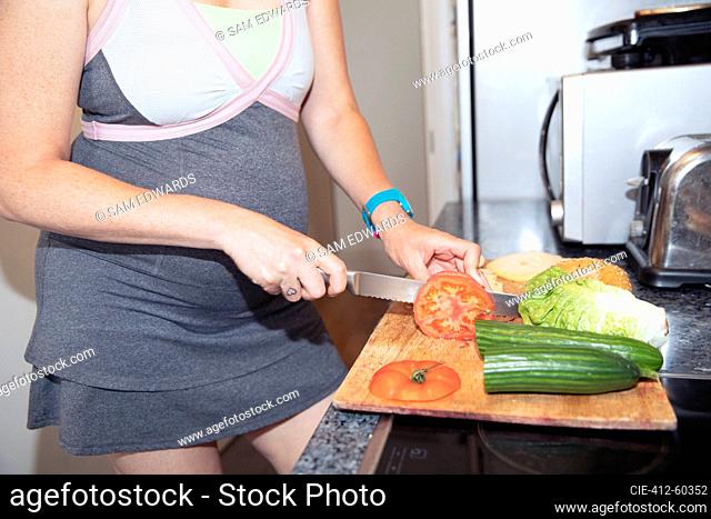 Pregnant woman slicing vegetables at cutting board in kitchen