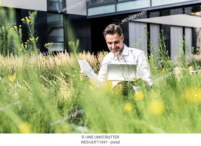 Smiling businessman working in grass outside office building