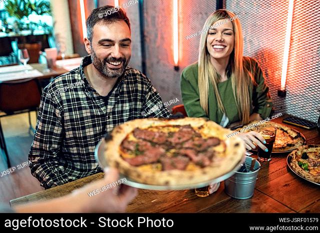 Woman offering pizza to male and female friends in restaurant