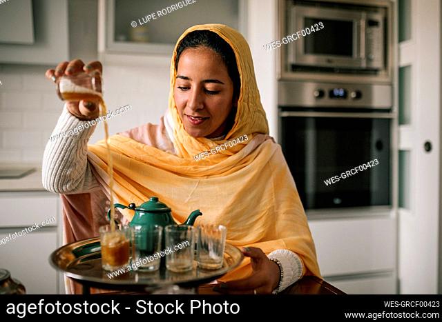 Young woman pouring tea in cup at home