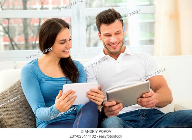Happy Young Couple Sitting On Sofa Using Digital Tablet