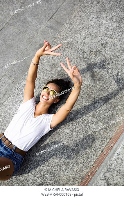 Happy young woman lying down doing V sign