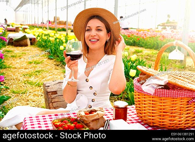 Attractive young woman having appetizer among tulip flowers. Fresh harvest with picnic and red wine in coutryside on spring time