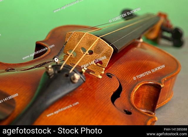 An old violin with slight scratches and damage in the bleed on a neutral, green background. | usage worldwide. - /Deutschland
