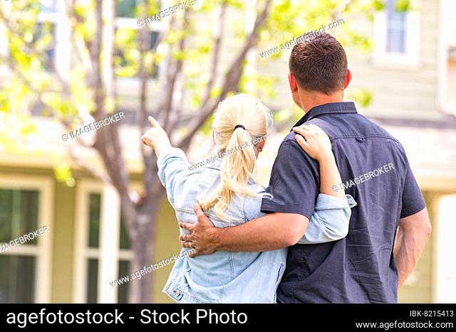 Happy caucasian couple facing and pointing to front of house