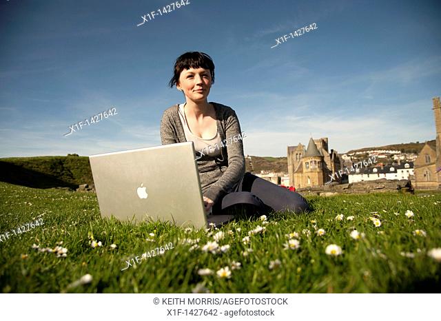 A young woman UK Aberystwyth university student working on her apple laptop computer outdoors on a sunny warm day