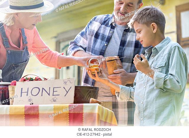 Grandparents and grandson tasting and selling honey at farmer’s market stall