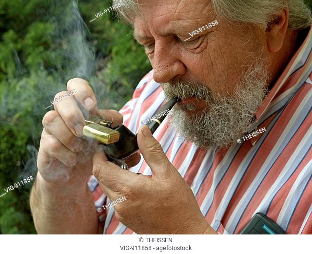 elder bearded man lighting his pipe with a cigarette lighter . - 27/04/2007