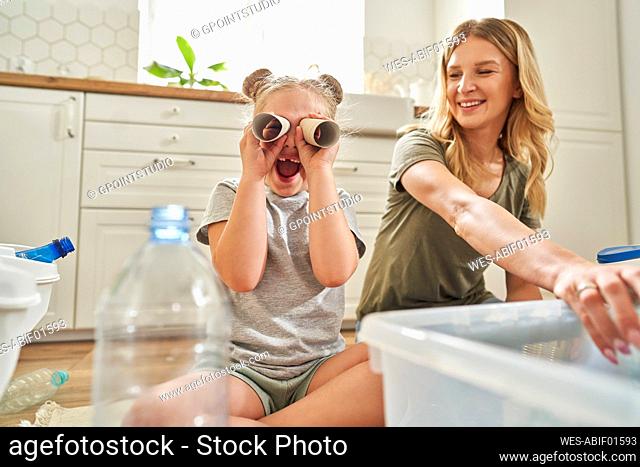 Cheerful daughter playing with rolled up paper while sitting by mother at home
