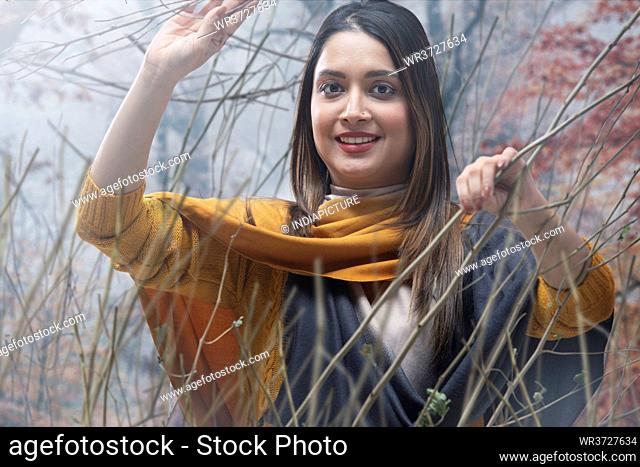 A HAPPY YOUNG WOMAN STANDING AMIDST DRIED BRANCHES