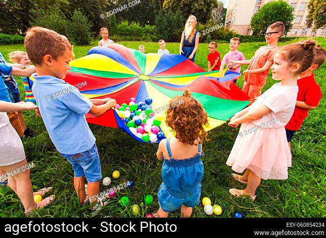 Close view kids having fun at summer birthday party. Games involving everyone. Activities for children of different age. Colorful parachute as game to unite and...