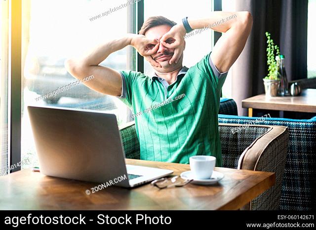 Young funny crazy businessman in green t-shirt sitting and looking with binoculars gesture. business and freelancing concept