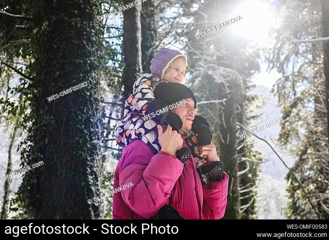Man wearing knit hat carrying daughter on shoulders in forest