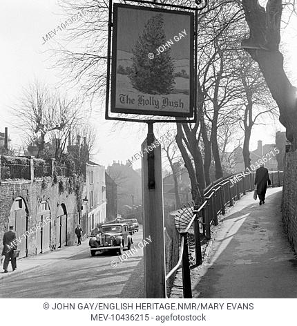The inn sign for the Holly Bush Inn in Hampstead at the junction of Holly Hill and the path up to Mount Vernon, with a woman walking up the slope to right