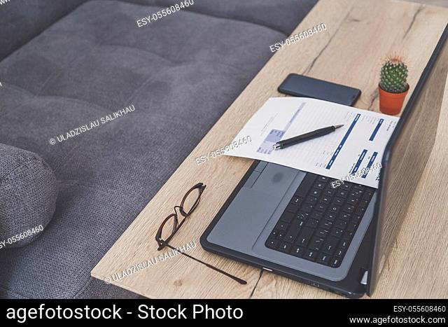 Home office desk workspace. Laptop, invoice and eyeglasses on wooden table