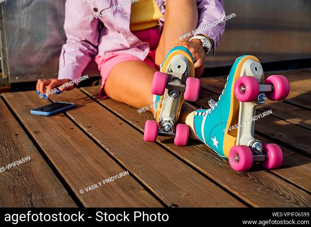 Woman wearing roller skates using mobile phone sitting on floorboard