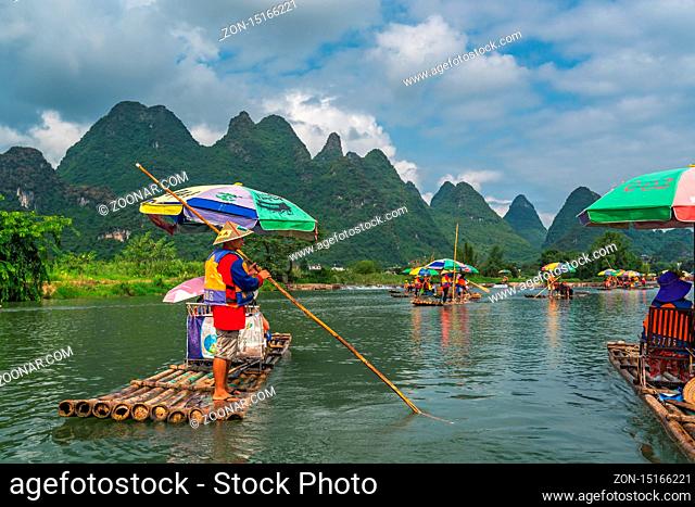 Yangshuo, China - August 2019 : Tourists sitting on bamboo rafts steered by guides with a long sticks on scenic and beautiful Yulong River