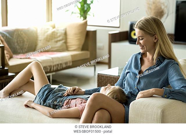Happy mother and daughter cuddling and relaxing on a couch in a modern living room