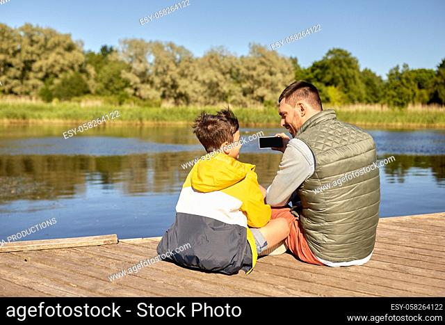 father and son taking selfie with phone on river