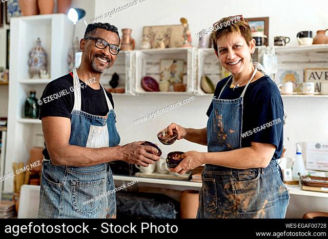 Smiling coworkers holding ceramics while standing in workshop