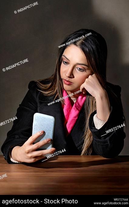 A YOUNG WOMAN IN WINTER CLOTHES SITTING AND USING MOBILE PHONE