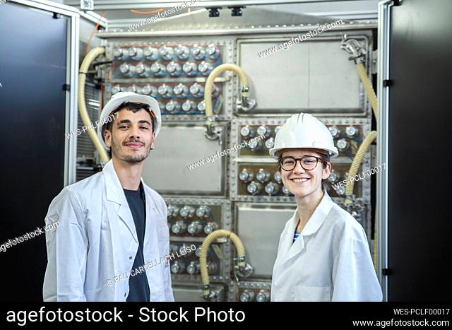 Smiling engineers with hardhat by machine in factory