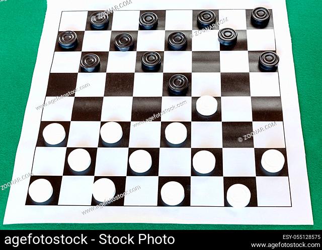 white checkered sheet board with draughts on green baize table