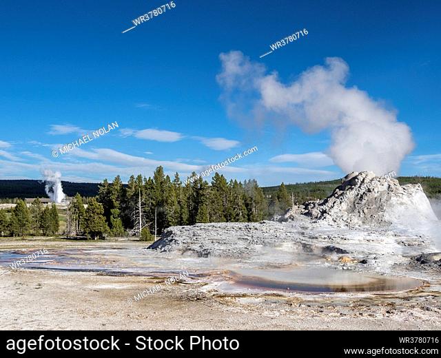 Castle Geyser steaming, with Old Faithful erupting behind, in Yellowstone National Park, UNESCO World Heritage Site, Wyoming, United States of America