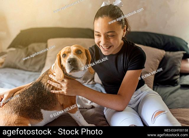 Cheerful girl looking at dog in bedroom