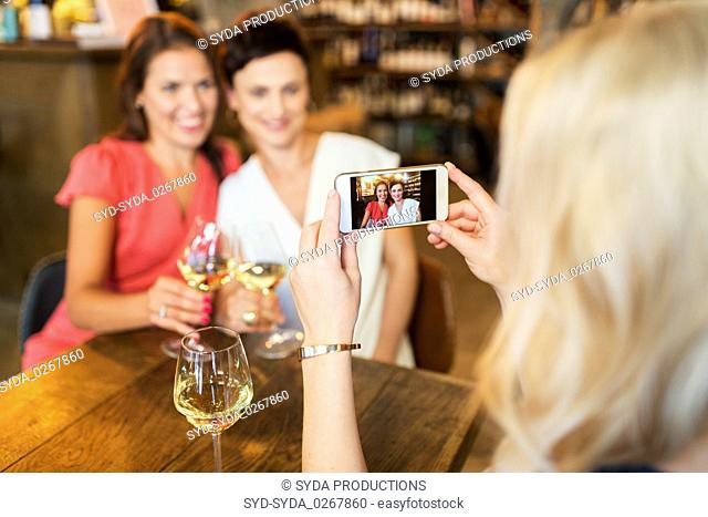 woman picturing friends by smartphone at wine bar