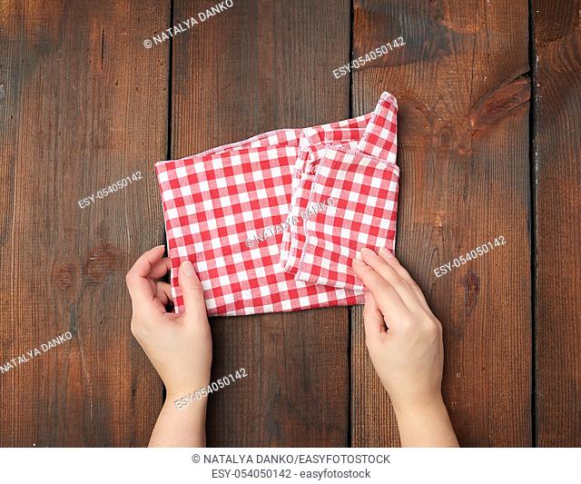 hands hold white red checkered kitchen towel on a brown wooden background, picnic background, top view