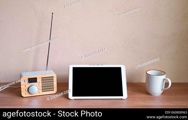 tablet computer with retro radio and coffee cup on desk - blank screen and wall with copy space