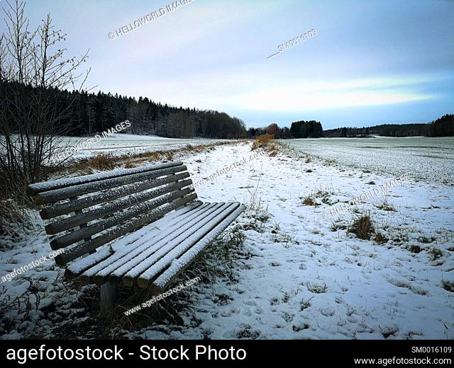 Ice and frost covered frozen bench seat in snow covered landscape, Sweden