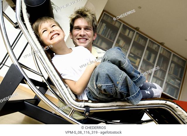 Low angle view of a son lying on a chaise longue with his father sitting beside him
