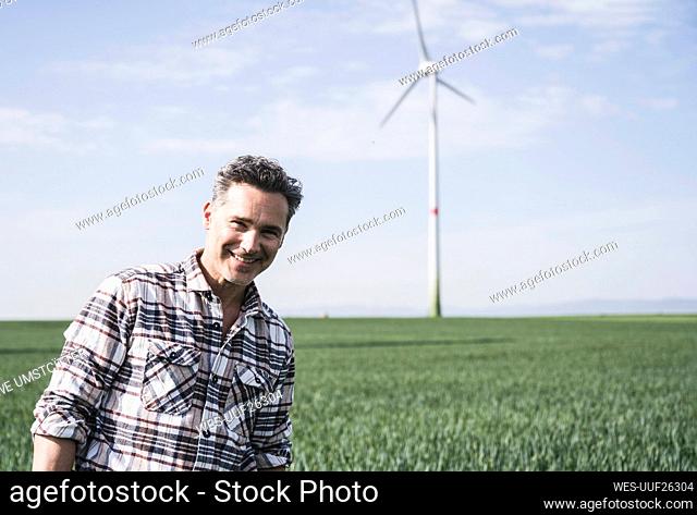 Happy mature engineer standing in front of wind turbine on sunny day