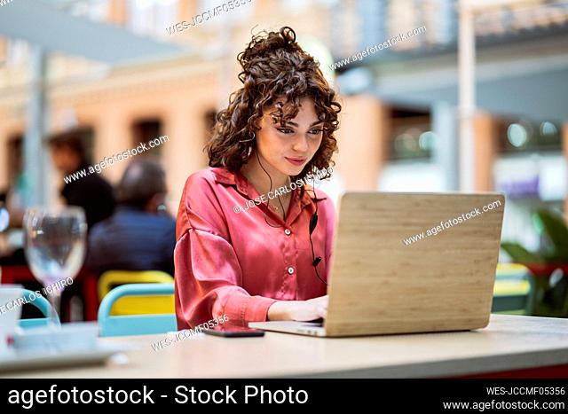 Young businesswoman freelancing on laptop at sidewalk cafe
