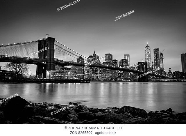 Brooklyn bridge and New York City Manhattan downtown skyline at dusk with skyscrapers illuminated over East River panorama. Copy space