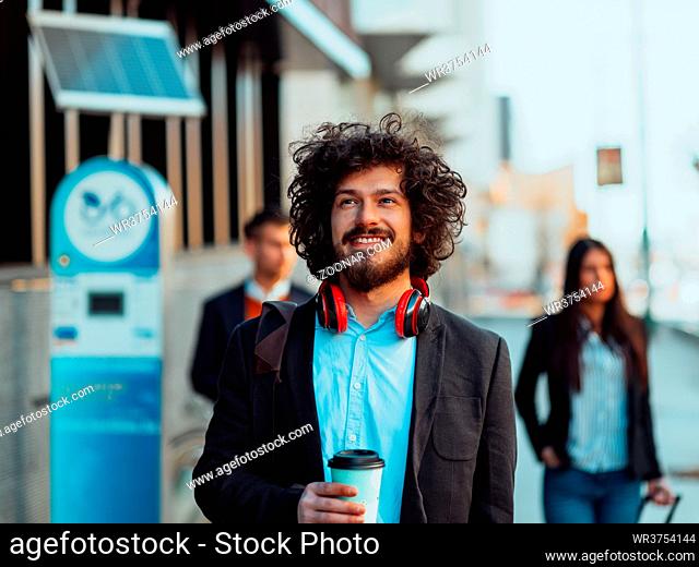 Happy student with afro haircut walking on campus while wearing his manbag and his headphones